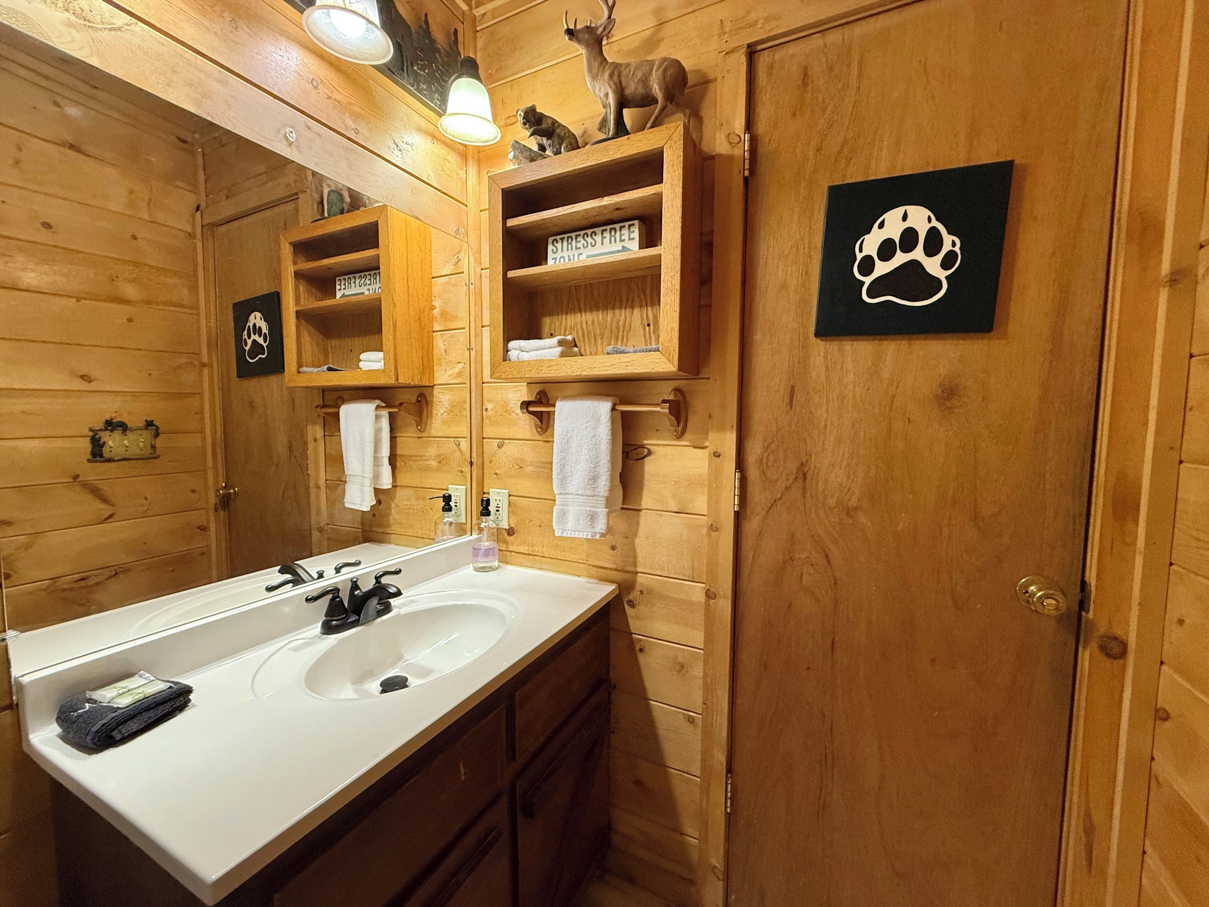 A wooden bathroom with a large mirror, two sinks, and shelves with towels and toiletries.