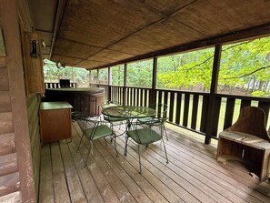 Una terrazza coperta all'aperto con tavolo e sedie di legno, un barbecue e vista su una foresta.