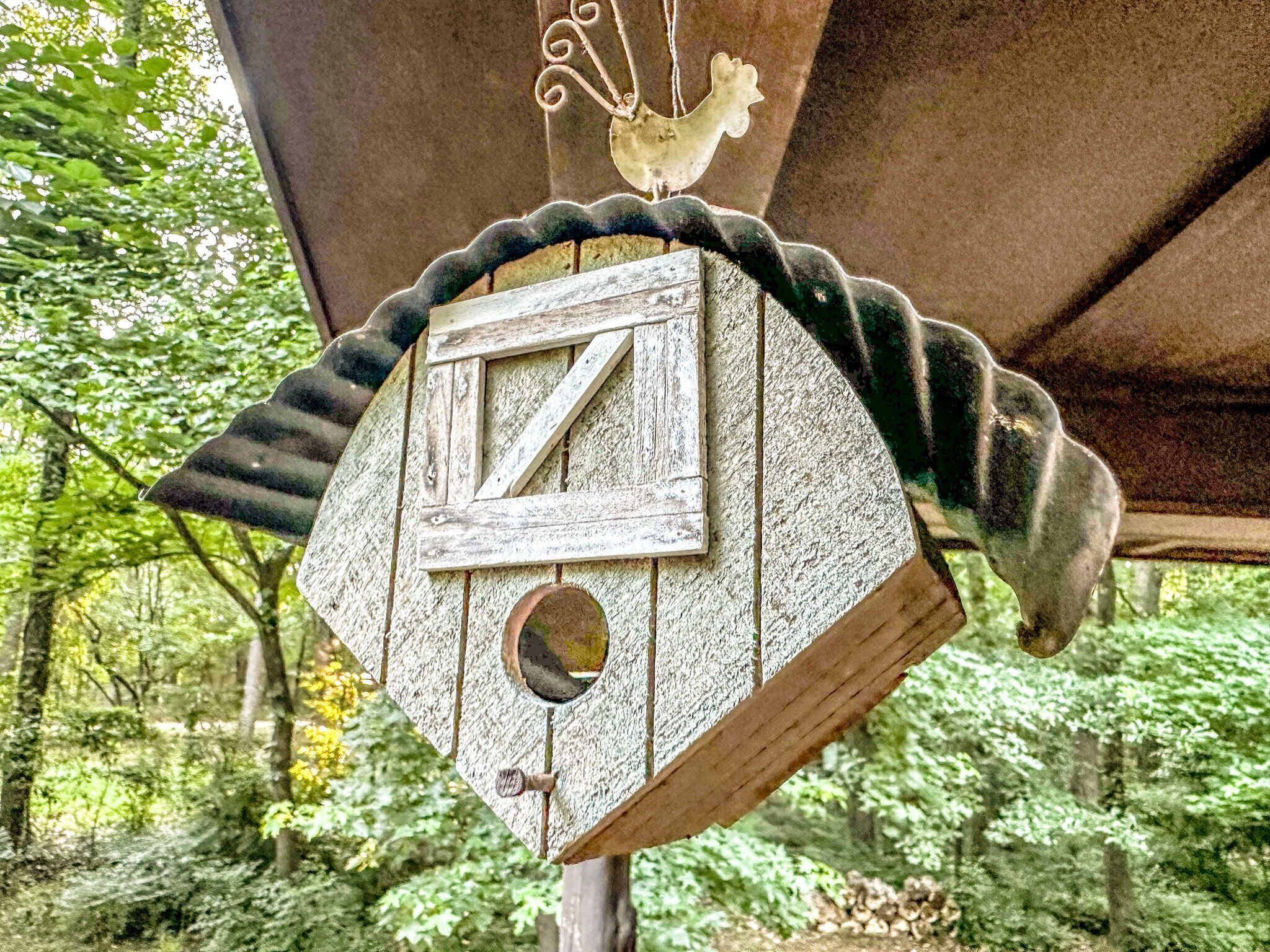 Une nichée à oiseaux en bois, portant le chiffre « 7 », suspendue à une structure dont le bord est décoré d’un motif festonné.