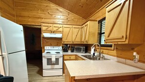 A compact kitchen with wooden cabinets, a white refrigerator, a stove, a microwave, and a sink.