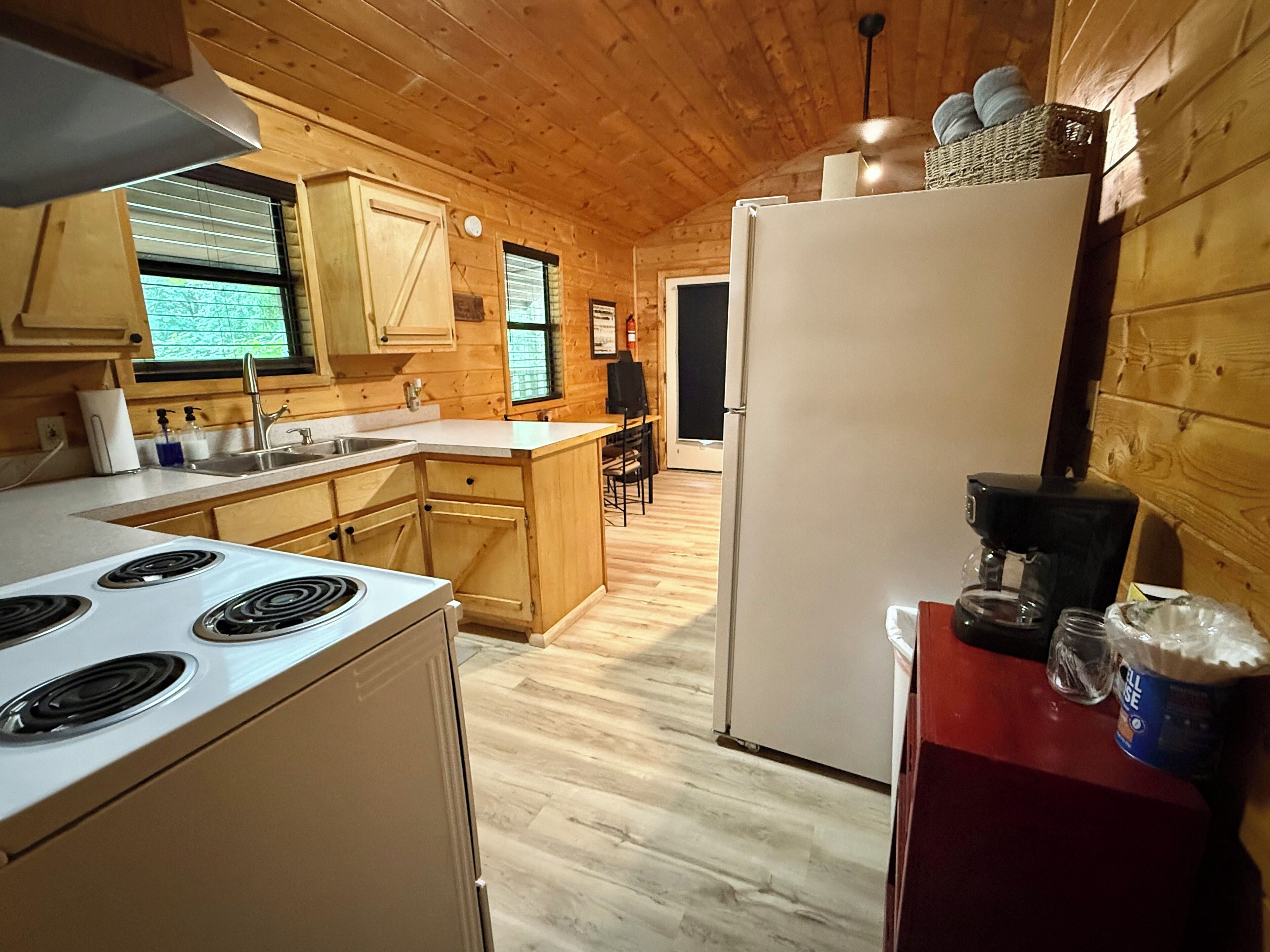 Interior de una cabaña de madera con cocina, que incluye estufa, pileta y refrigerador.
