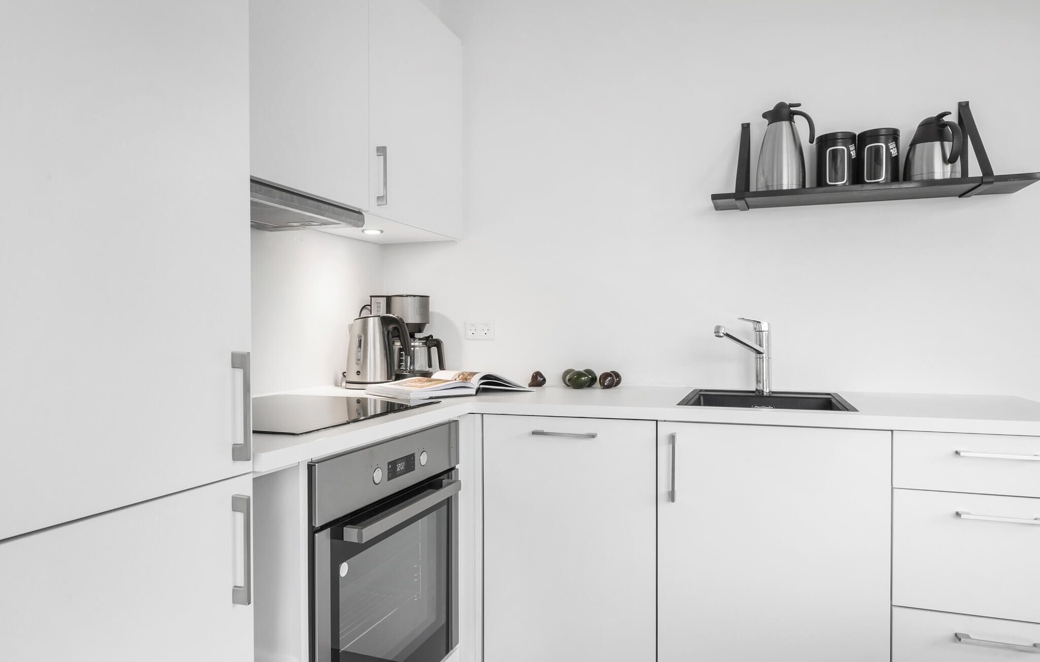 A modern kitchen with white cabinetry, a built-in oven, a coffee maker, and a sink.