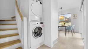 A modern laundry room with a stacked washer and dryer, wooden stairs, and a view to a dining area with a table and chairs. - Awesome apartment in Slagelse with WiFi (Slagelse)