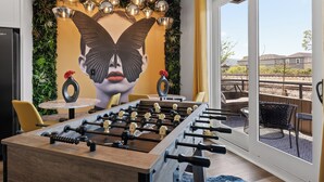 A foosball table in a room with a mural of a woman's face, a round table, and chairs.