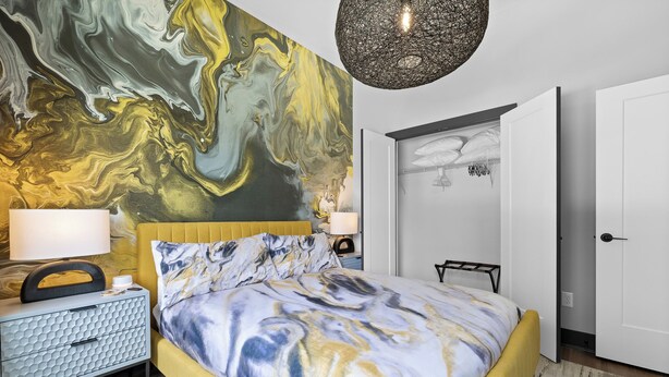 A modern bedroom with a marble-patterned bedspread, a geometric-patterned nightstand, and a large abstract mural on the wall.