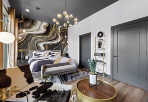 A modern bedroom with a marble-patterned headboard, a round coffee table, a sofa, and a bedside table with a plant.