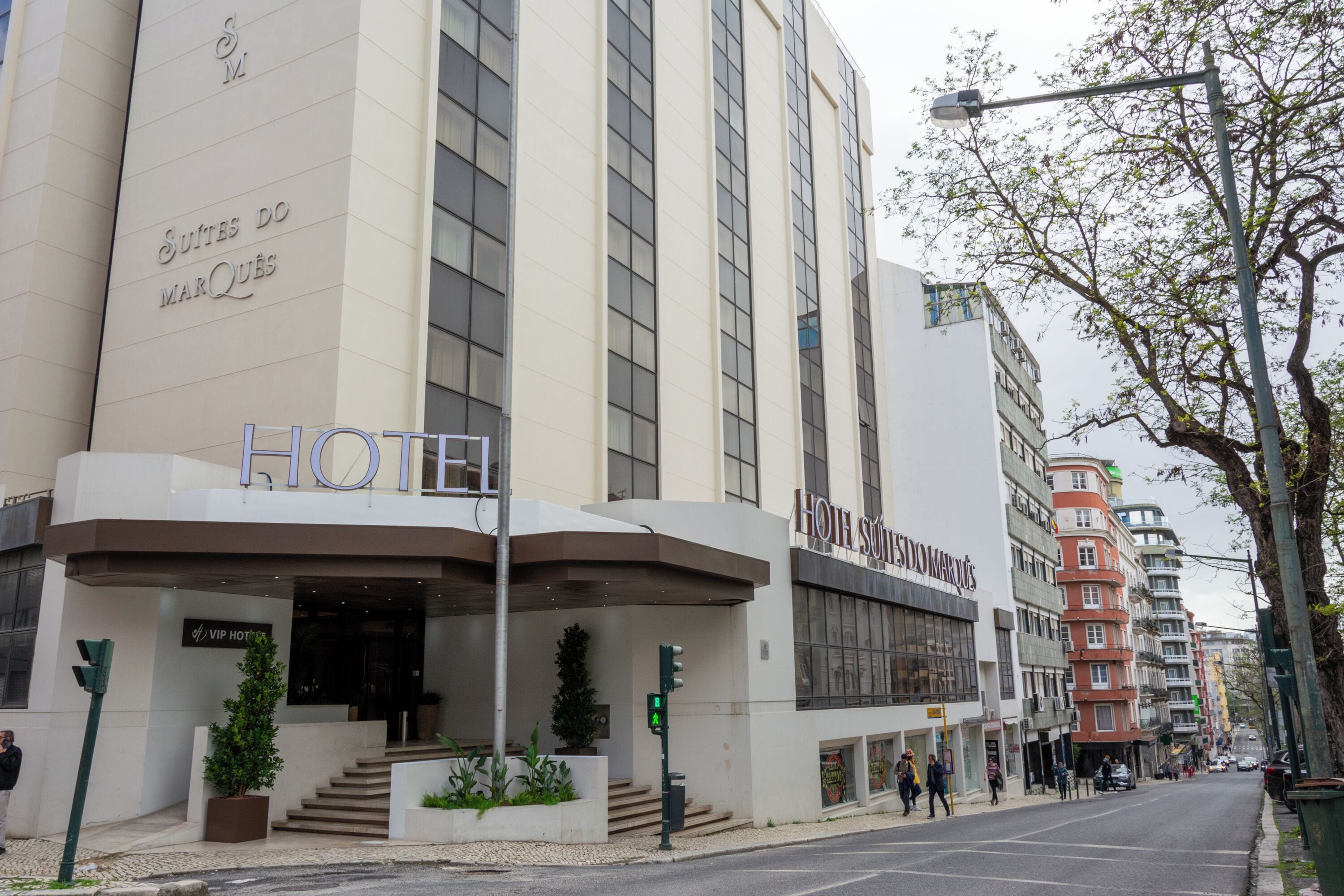 A modern hotel with a prominent entrance, a staircase leading to the lobby, and a clear view of the street.