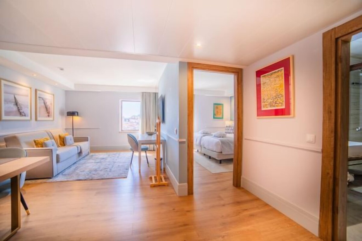 Ein modernes Wohnzimmer mit einer Couch, einem Esstisch und einem Fernseher. Ein Flur führt zu einem weiteren Zimmer mit einem Bett.