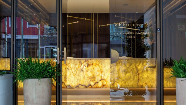 A hotel reception area with a marble counter, glass doors, and potted plants. - VIP Executive Suites do Marques Hotel (Lisbon)
