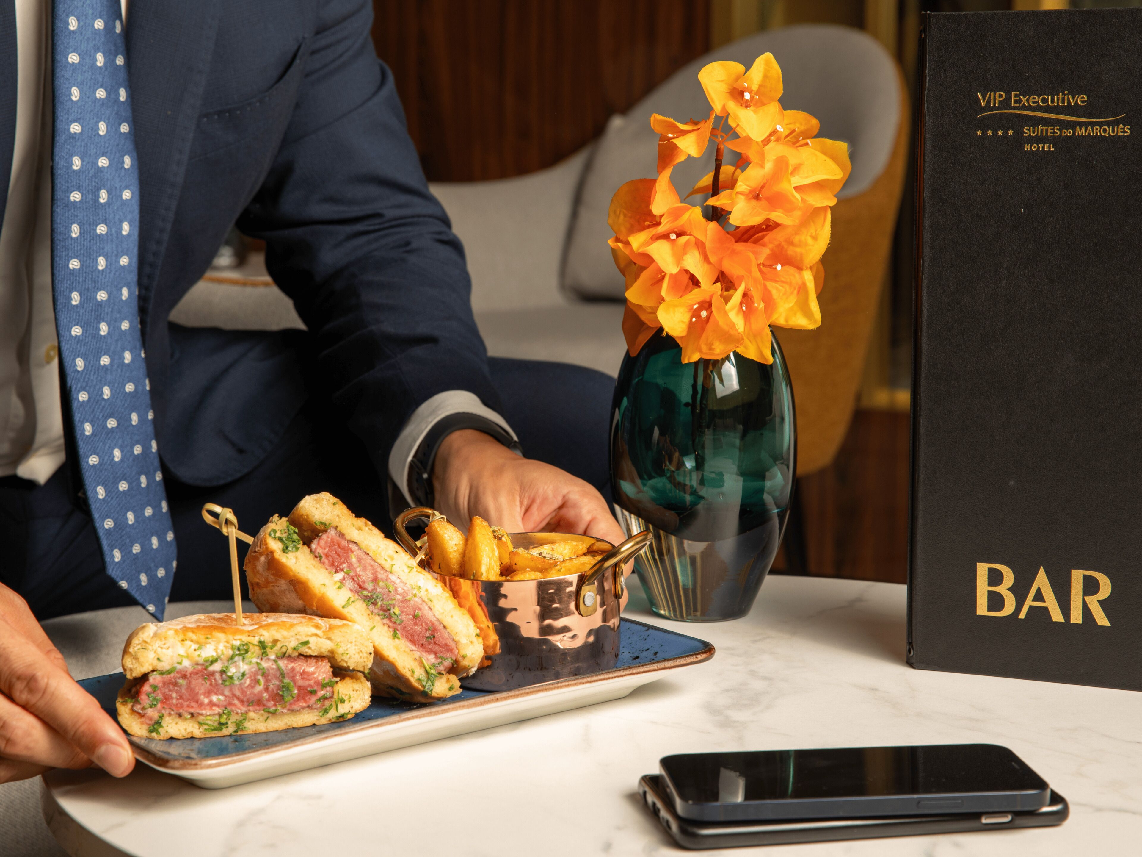 A dining table with a sandwich, a vase of flowers, and a menu.
