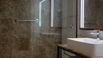 Une salle de bain moderne avec une douche à parois de verre, un mur recouvert de carreaux de marbre, un lavabo blanc et un grand miroir.