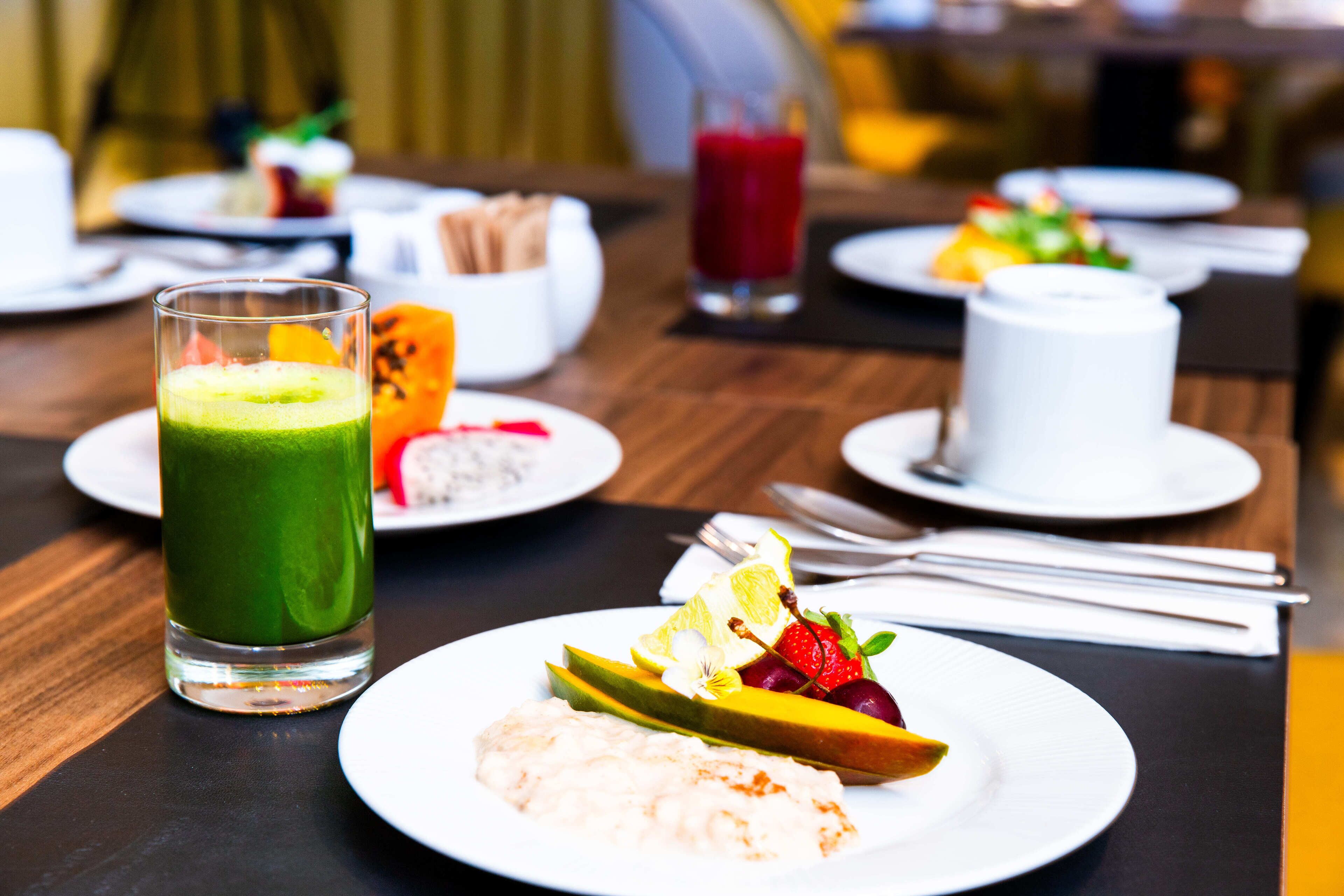 Une table à manger avec des assiettes de nourriture, un verre de smoothie vert et une tasse blanche.