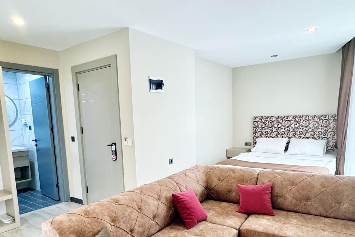 Une chambre d’hôtel moderne avec un grand canapé d’angle marron, une table en bois et un lit doté d’une tête de lit à motifs.