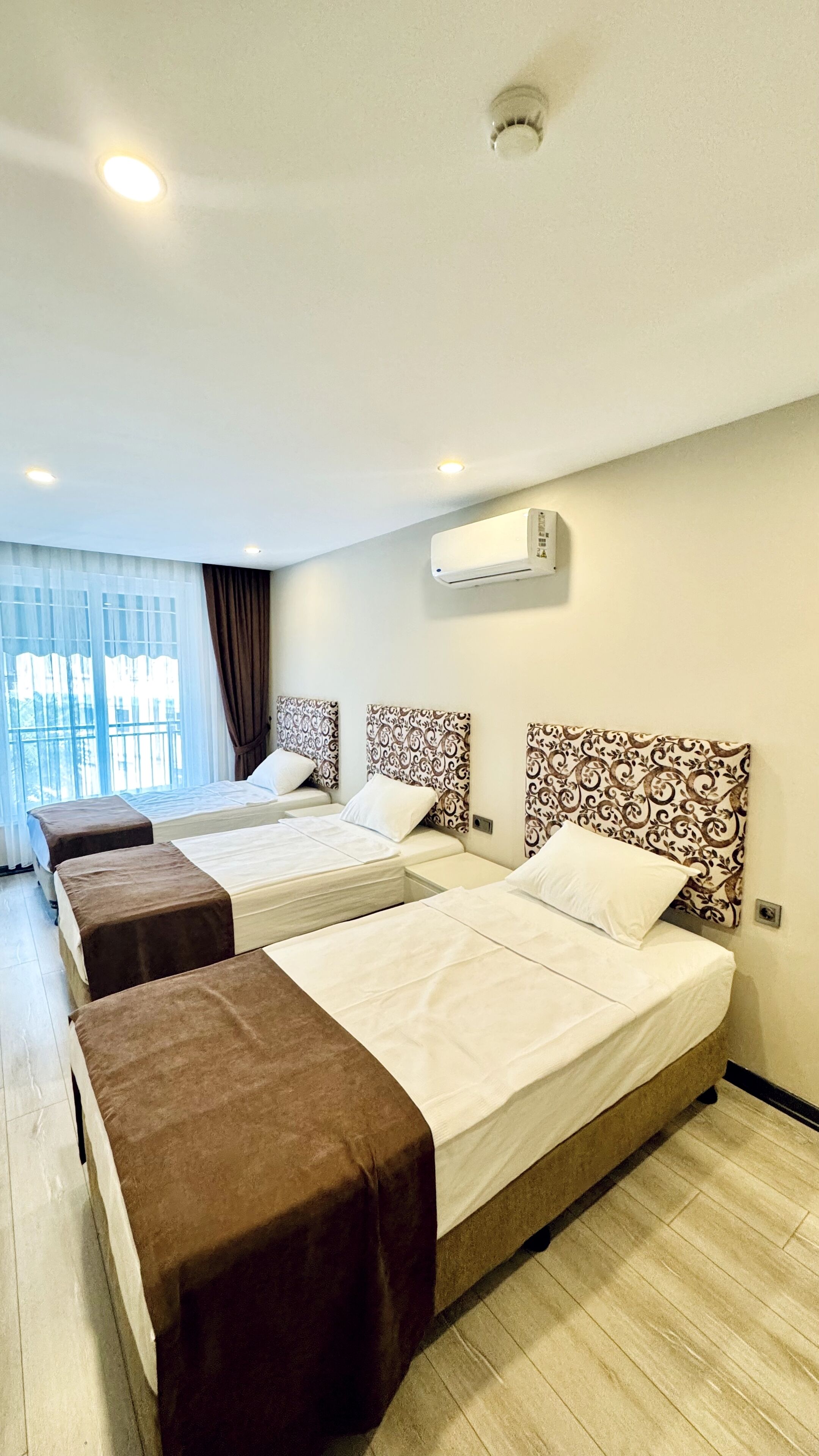 Une chambre d’hôtel avec deux lits, une fenêtre avec des rideaux, un appareil de climatisation et un luminaire au plafond.