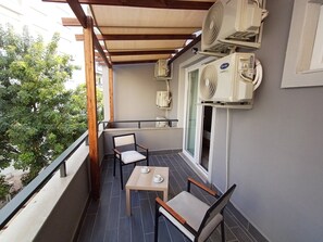 Een balkon met twee stoelen, een tafel en twee airconditioners.