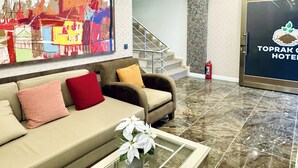 Um lobby de hotel moderno com um sofá, uma mesa de centro de vidro, uma pintura abstrata colorida, uma escada e um balcão de recepção.