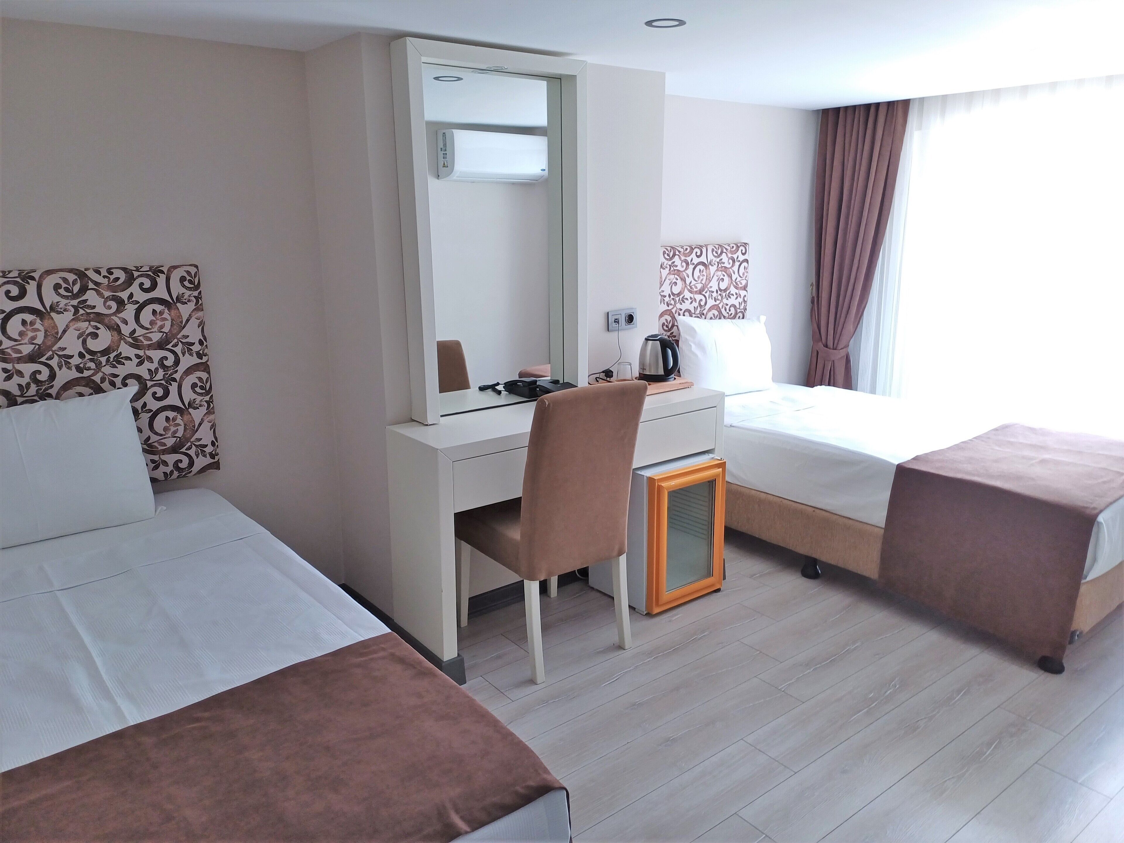 Habitación de hotel con dos camas, un escritorio, una silla, una mesita con hervidor y un espejo.