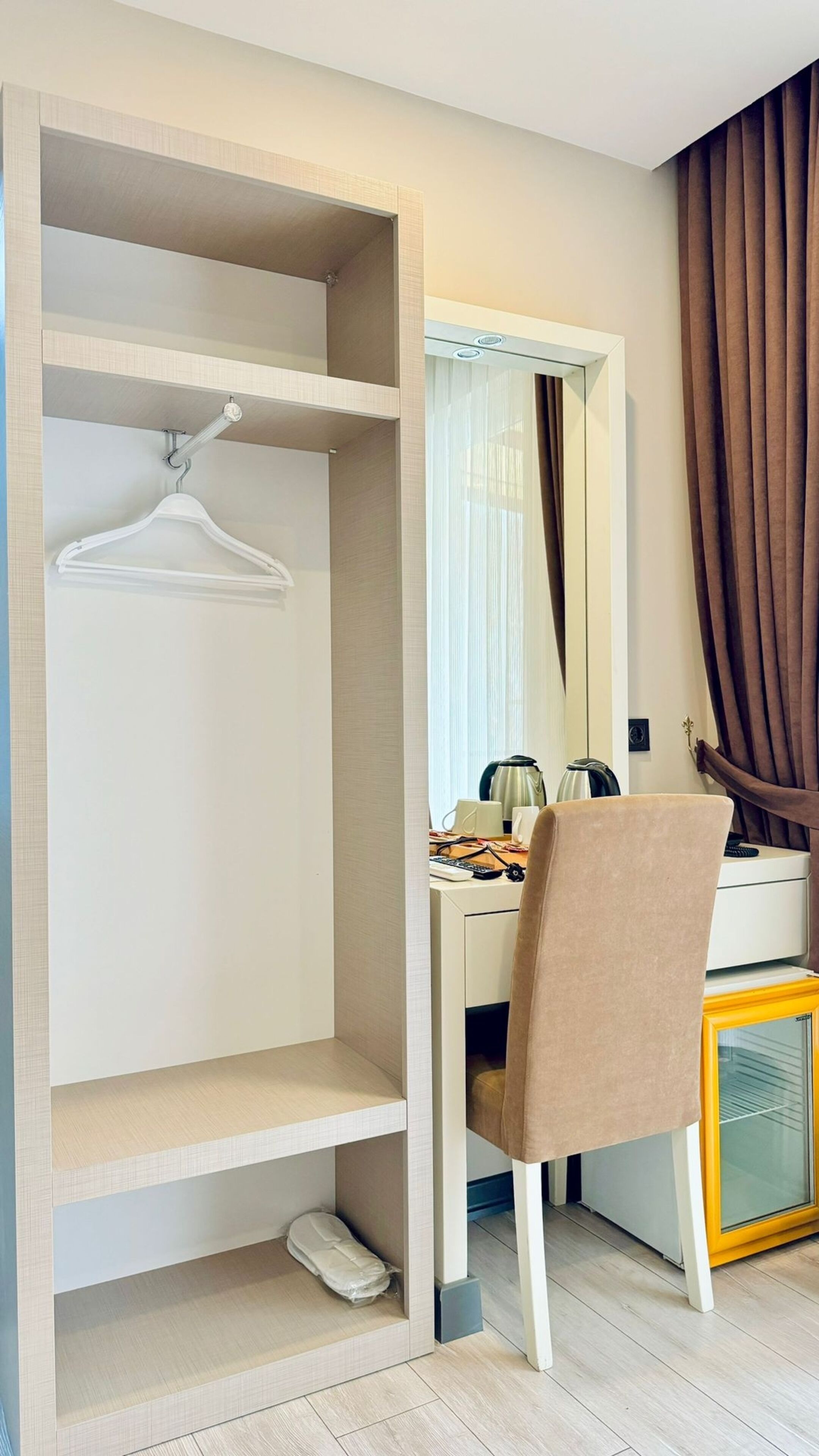 Una habitación moderna con un escritorio blanco, una silla, un espejo, un armario con organizador colgante y un mueble amarillo.
