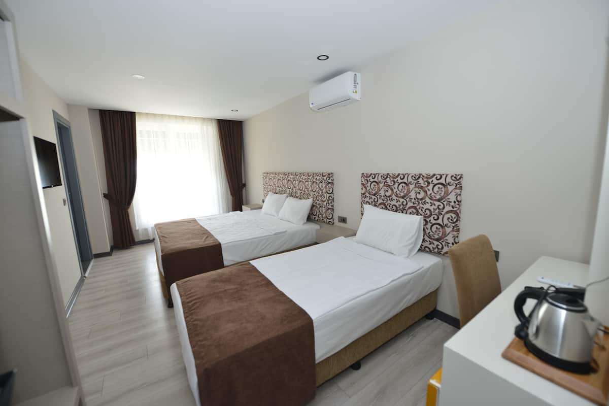 Une chambre d’hôtel avec deux lits, un bureau, une chaise, une bouilloire et un appareil de climatisation.