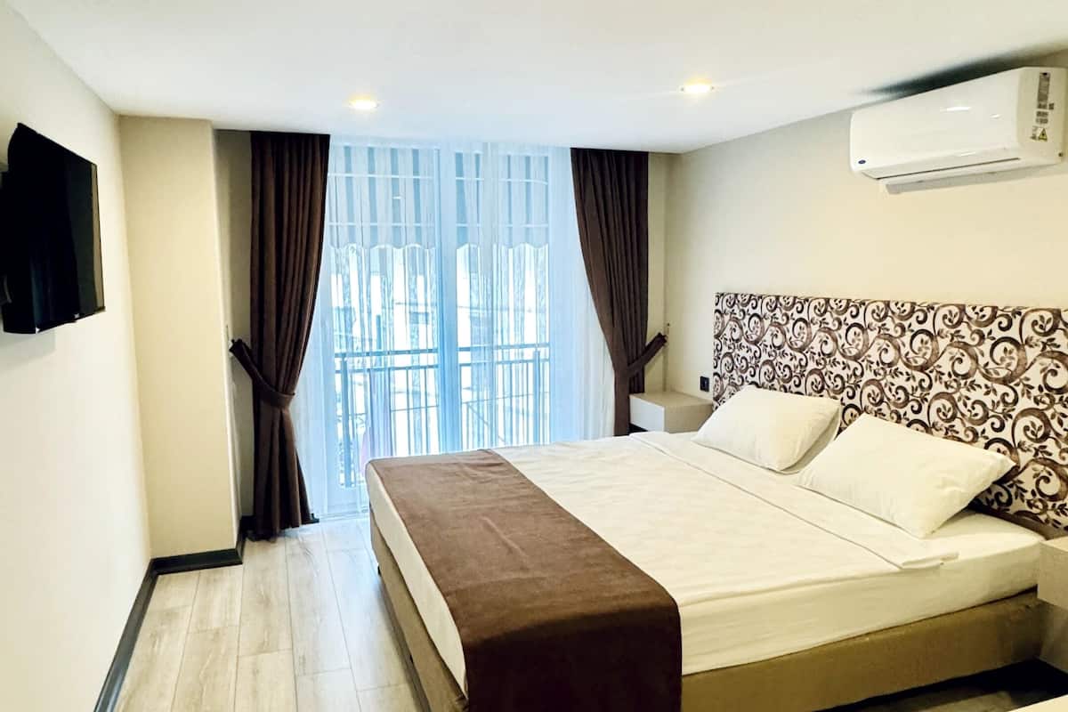 Une chambre d’hôtel avec un lit, une table de chevet, un téléviseur fixé au mur et une fenêtre avec des rideaux.