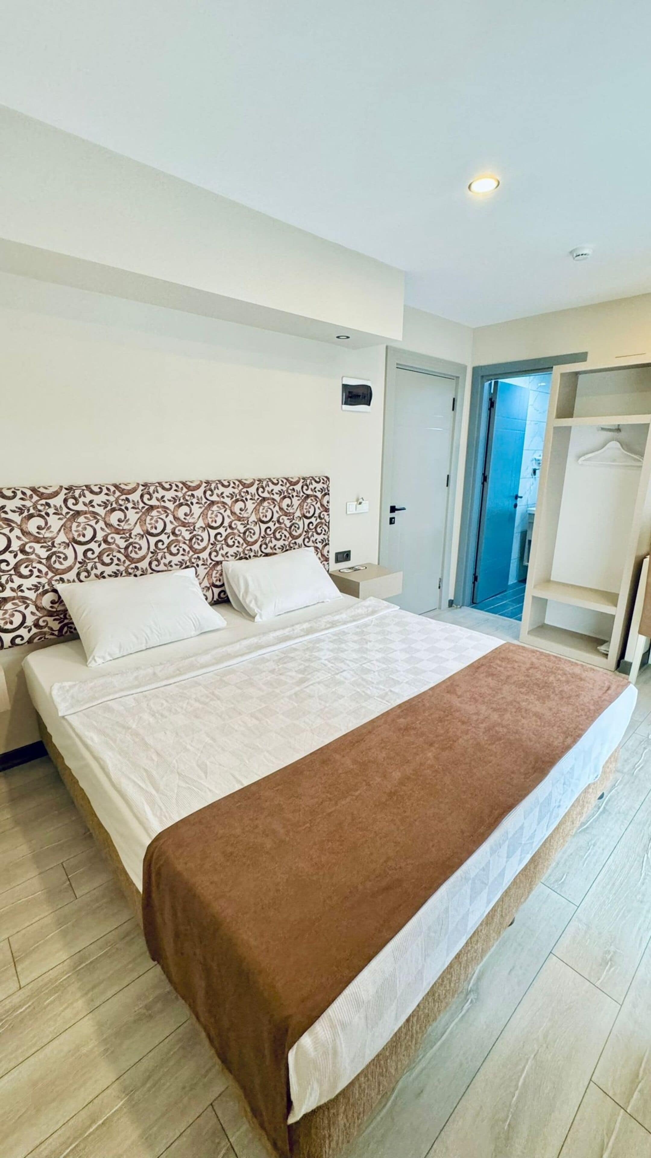 A hotel room with a large bed, a patterned headboard, a bedside table, and a wardrobe.