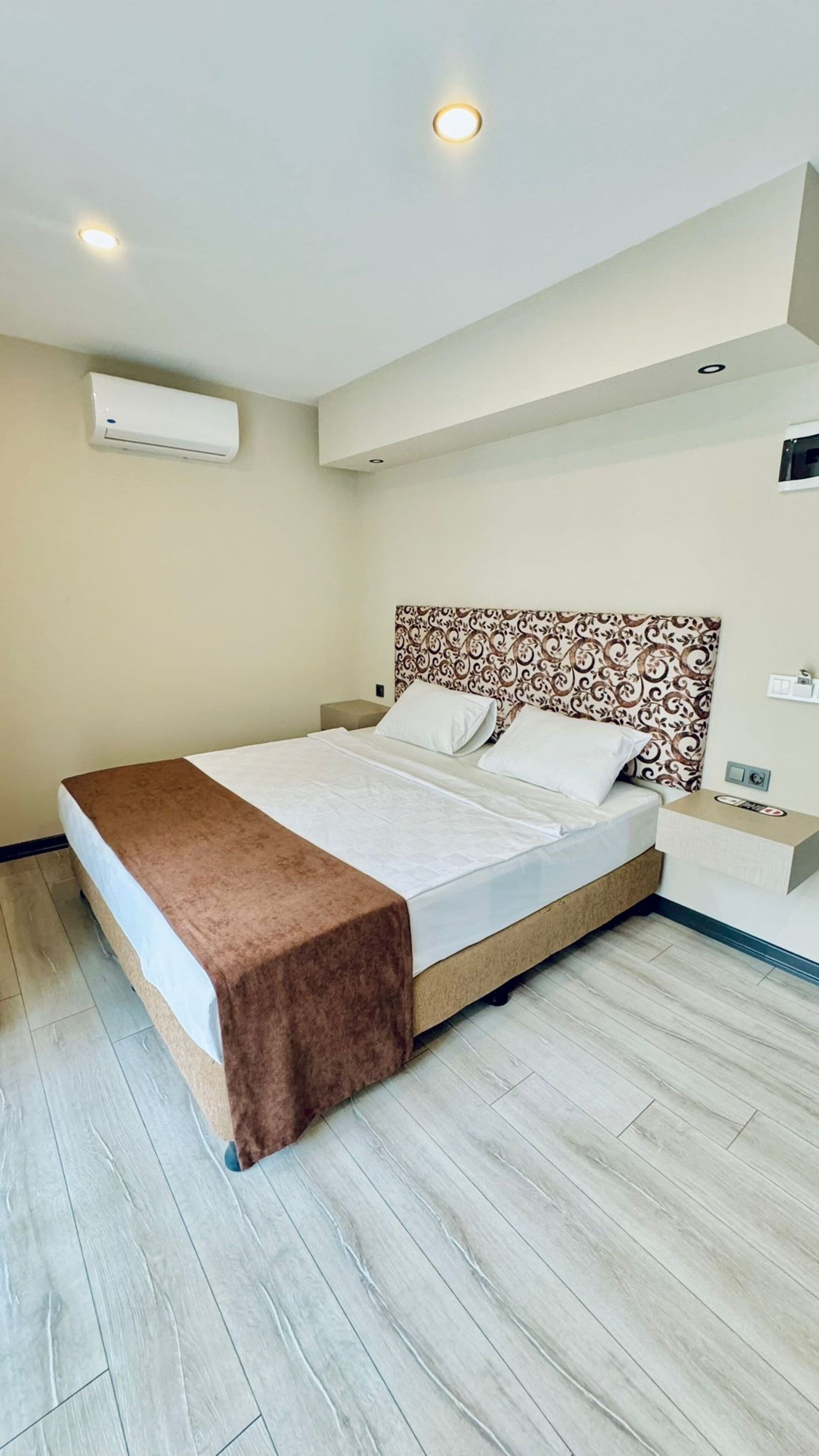 Een moderne slaapkamer met een bed, nachtkastjes, een gestreept hoofdeinde en inbouwspots.