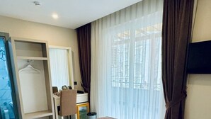 Quarto de hotel com uma cama grande, uma escrivaninha, uma cadeira, um guarda-roupa e uma televisão na parede.