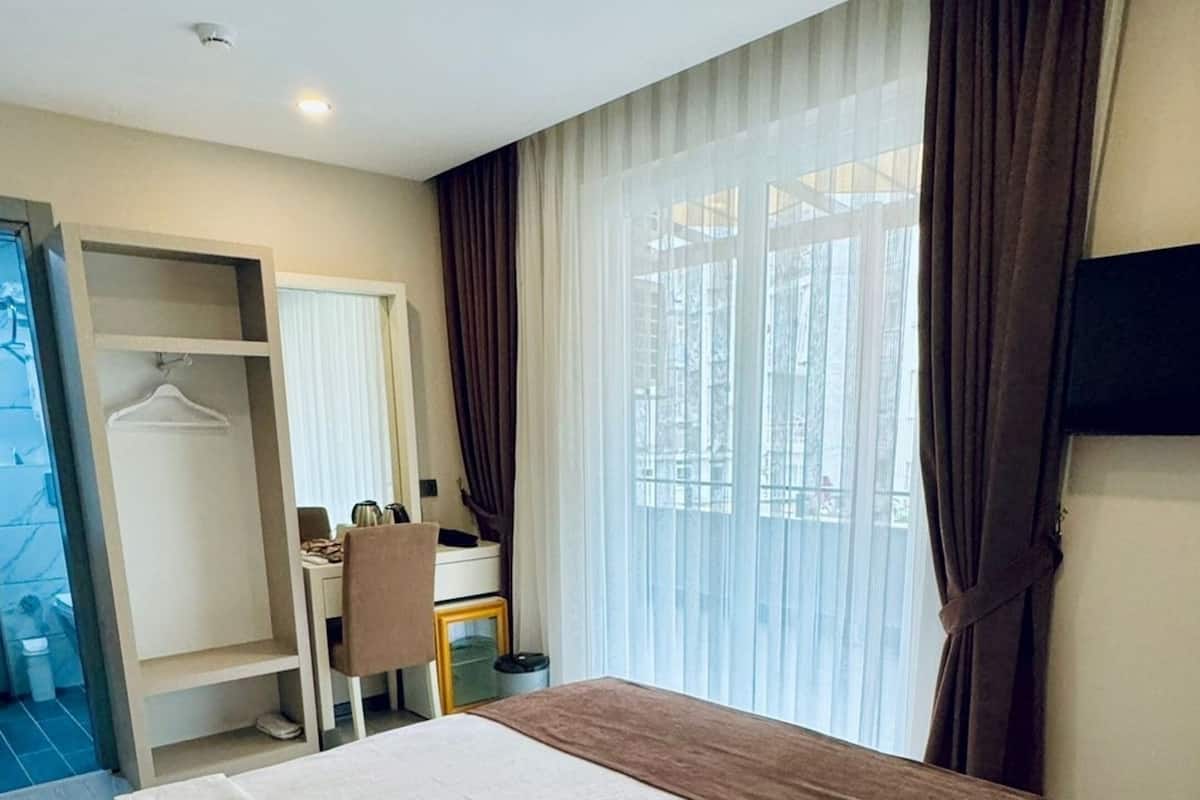 Une chambre d’hôtel avec un grand lit, un bureau, une chaise, une armoire et un téléviseur fixé au mur.