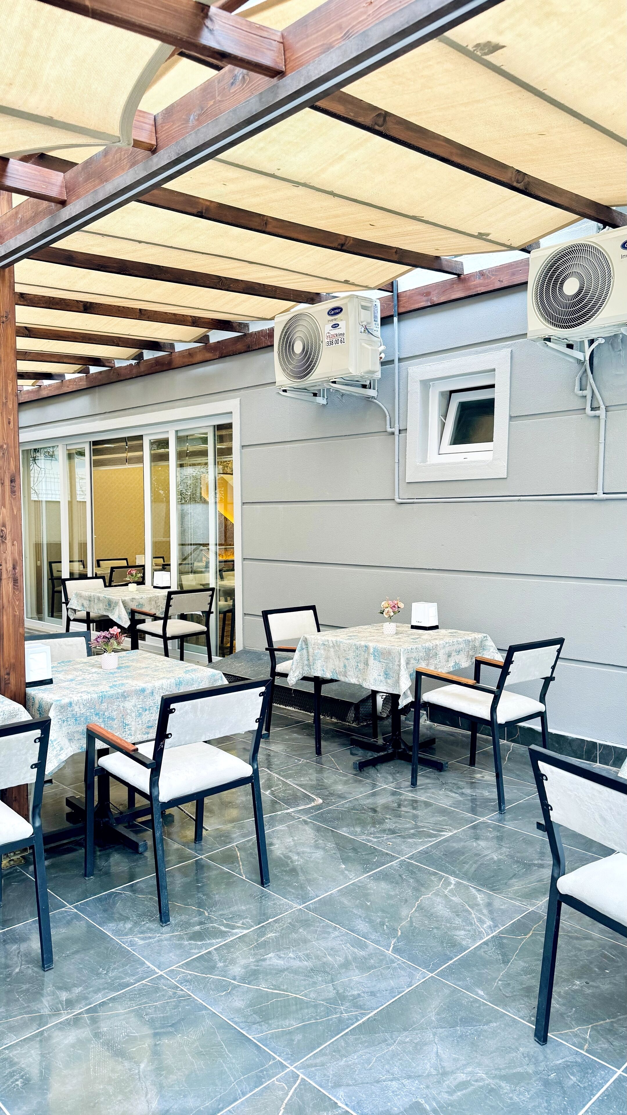 Eine Außenpatio mit Tischen und Stühlen, überdacht von einer Holzpergola und ausgestattet mit Deckenventilatoren.