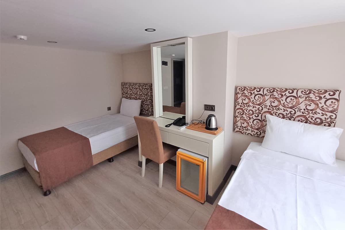 Une chambre d’hôtel avec deux lits, un bureau, une chaise, un miroir et un petit placard.