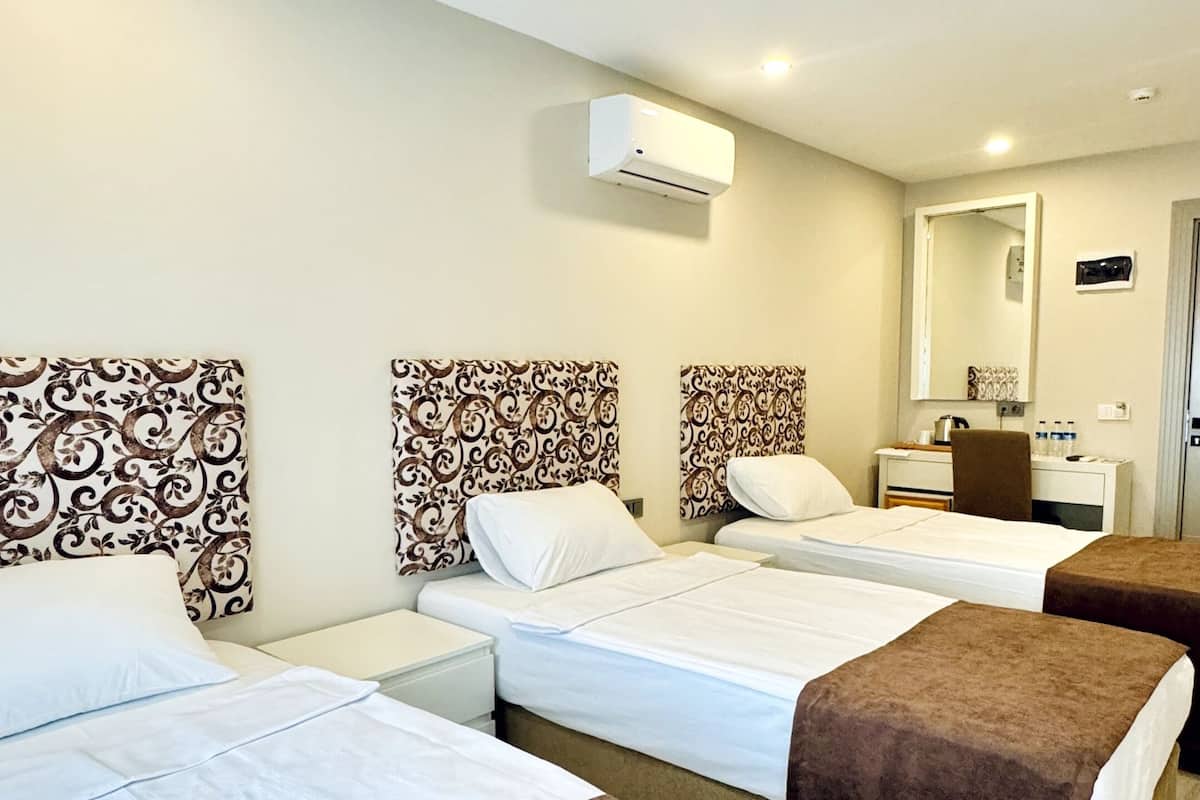 Une chambre d’hôtel avec trois lits, chacun doté d’une tête de lit marron et de draps blancs. Un climatiseur mural est fixé au-dessus des lits.