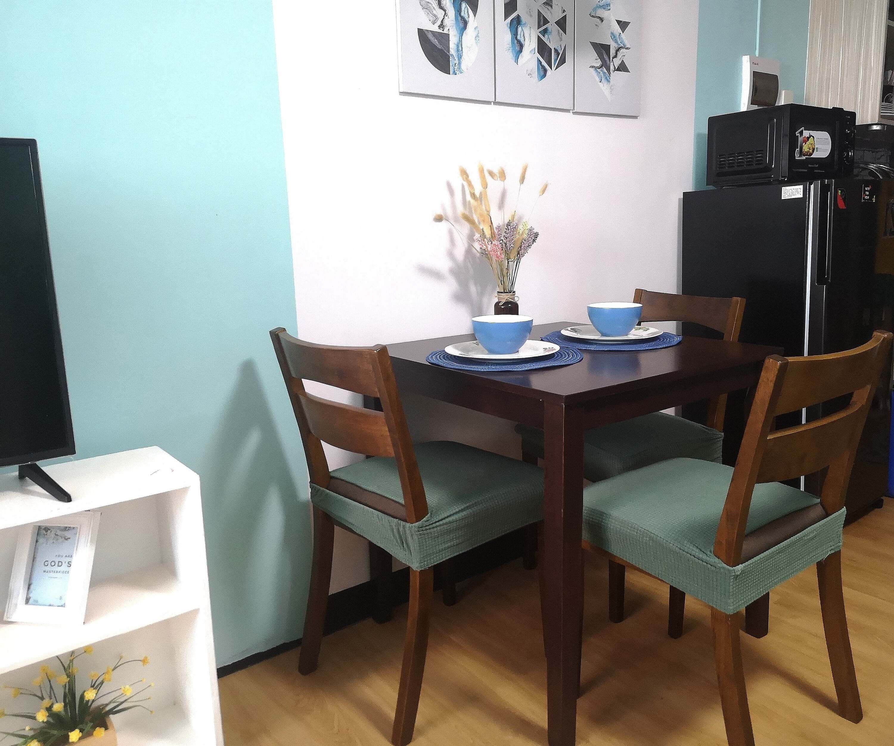 Un coin repas avec une table en bois, deux chaises dotées de coussins verts et un vase contenant des fleurs séchées.