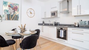 A modern kitchen with white cabinets, a microwave, a toaster, and a gas stove. There is a dining table with black chairs and a glass top. - Premier Three Bedroom Bliss City View Shoreditch (London)