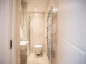 A modern bathroom with a glass shower enclosure, a white toilet, and a built-in towel rack.