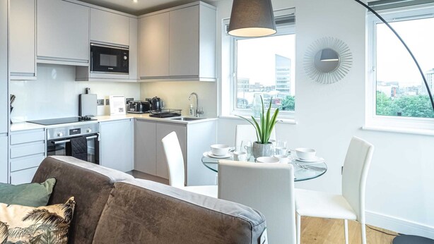 A modern kitchen with a dining area, a sofa, and a view of the city. - One Bed Near Windsor Castle by Belvilla (Slough)