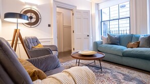 A living room with a blue sofa, grey armchairs, a wooden coffee table, and a floor lamp. - Liverpool St Three Bedroom Home Near Tube Station (London)