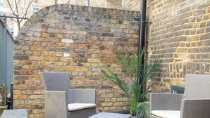 An outdoor patio area with wicker furniture and a brick wall. - Liverpool St Three Bedroom Home Near Tube Station (London)