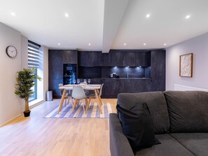 A modern living room with a grey sofa, a dining table set with plates and glasses, a kitchen with dark cabinets, and a potted plant. - Broadway Market Beauty Three-bedroom by Sojo Stay (London)