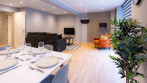 Uma sala de estar moderna com um sofá, uma mesa de jantar posta para quatro pessoas, uma TV e uma planta.