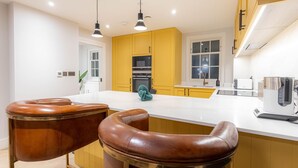 A modern kitchen with yellow cabinets, a white countertop, and two leather bar stools. - Three Bedroom Near Brick Lane by Belvilla (London)