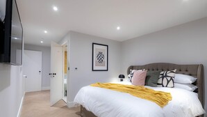 A modern bedroom with a large bed, a television mounted on the wall, and a door leading to another room. - Three Bedroom Near Brick Lane by Belvilla (London)