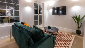 A modern living room with a green sofa, a small round table, a checkered rug, and a TV on the wall. - Three Bedroom Near Brick Lane by Belvilla (London)