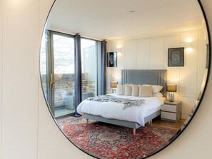 A bedroom with a bed, nightstands, a lamp, and a view through a glass door. - Five Bedroom Near Camden Arts Centre by Bevilla (London)