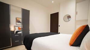 A modern bedroom with a bed, a wardrobe, a mirror, and a door. - Discover Angel Central Two Bedroom by Belvilla (London)