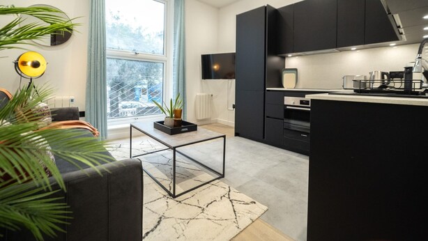 A modern kitchen with dark cabinets, a central island, and a dining area with a sofa and coffee table. - Discover Angel Central Two Bedroom by Belvilla (London)