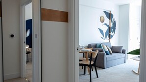 Una sala moderna con un sofá gris, una mesa de comedor con sillas y un espejo grande.