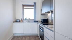 Una cocina compacta con armarios blancos, una ventana, microondas y un lavamanos.