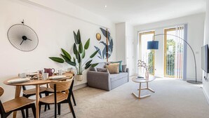 Una sala de estar moderna con comedor, un sofá gris, una planta grande y un televisor.