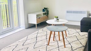 A modern living room with a white sofa, a round coffee table, and a TV mounted on the wall.