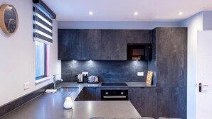 A modern kitchen with dark cabinetry, a built-in microwave, and a large island with a sink. - Victoria Park Vista One-bedroom by Sojo Stay (London)